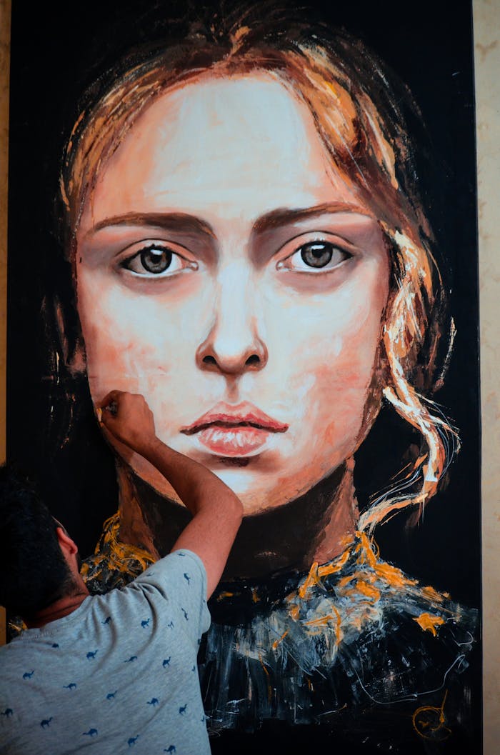 An artist meticulously paints a large portrait of a woman on canvas in an indoor art studio.
